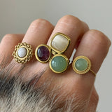 Tendance stacking : zoom sur trois bagues dorées différentes (pierre blanche, verte et trio multicolore) portées ensemble sur la même main.