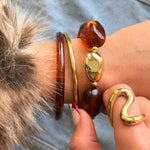 Bracelet à perles ambrées porté en accumulation avec des joncs dorés fins et une bague vague pour un look tendance.