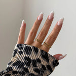 Bague nœud Alberta portée en accumulation (stacking) avec d'autres bagues fines dorées sur une main avec pull léopard.