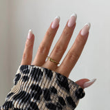 Bague nœud Alberta portée en accumulation (stacking) avec d'autres bagues fines dorées sur une main avec pull léopard.