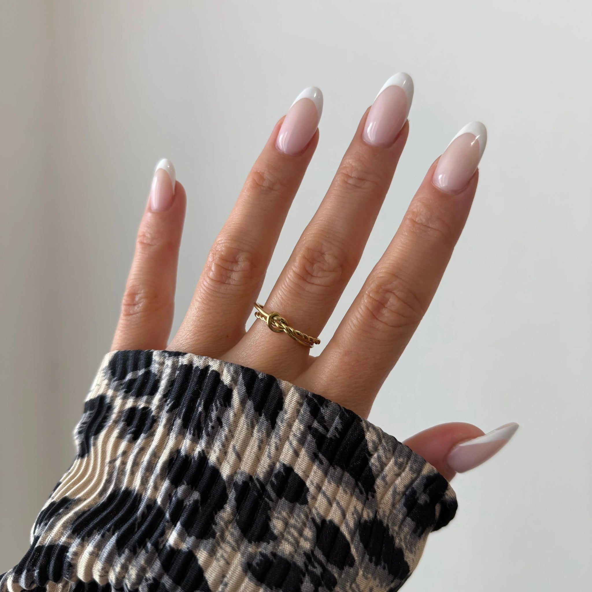 Bague nœud Alberta portée en accumulation (stacking) avec d'autres bagues fines dorées sur une main avec pull léopard.
