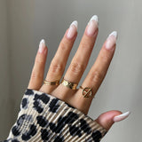 Bague fine Alessia portée en accumulation (stacking) avec d'autres bagues géométriques dorées sur une main avec pull léopard.