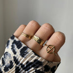 Bague fine Alessia portée en accumulation (stacking) avec d'autres bagues géométriques dorées sur une main avec pull léopard.