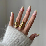 Bague graphique Alexandra portée en accumulation (stacking) avec d'autres bagues dorées fluides pour un look 'métal liquide' tendance.