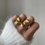 Bague graphique Alexandra portée en accumulation (stacking) avec d'autres bagues dorées fluides pour un look 'métal liquide' tendance.