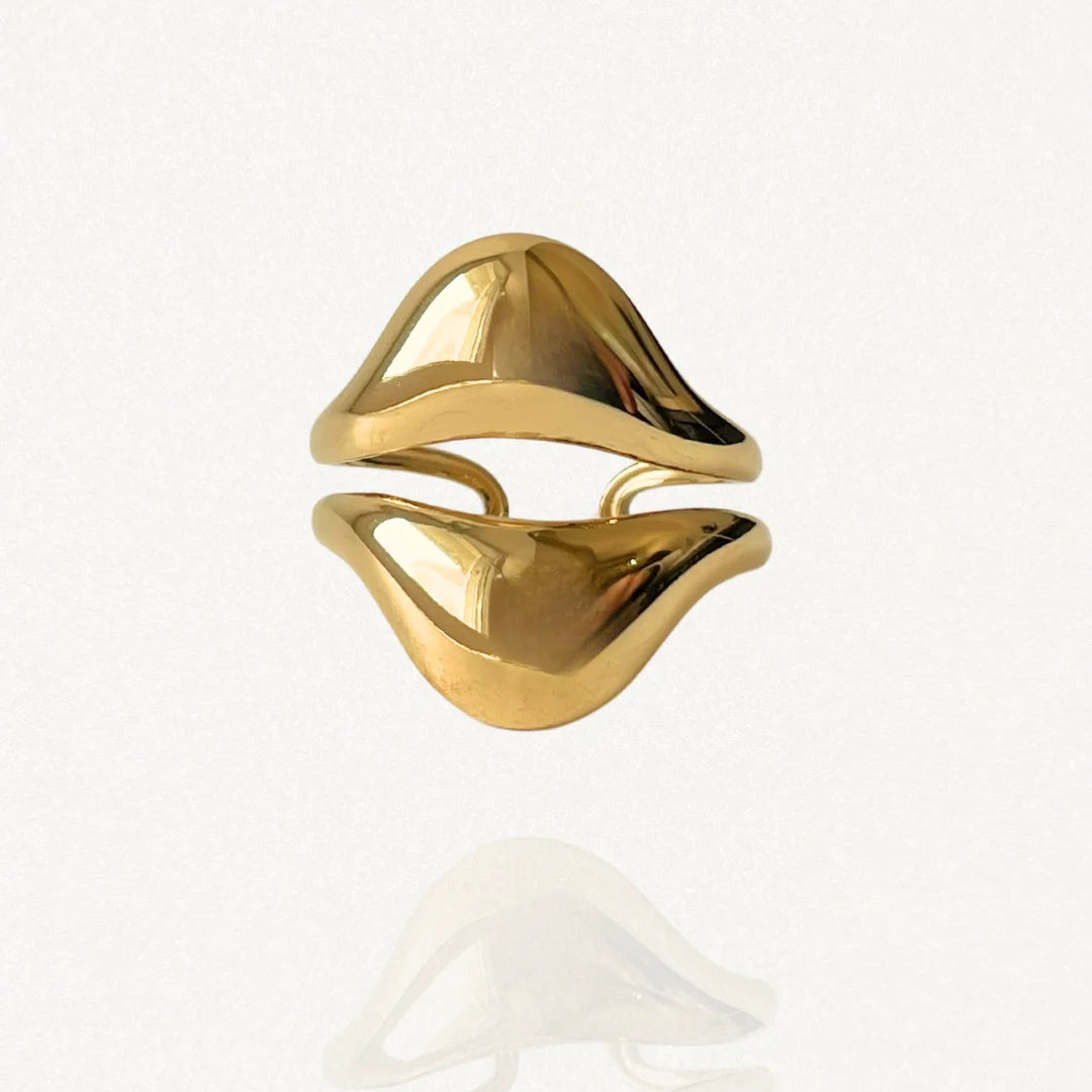 Bague large ouverte en acier inoxydable doré au design organique et fluide évoquant deux vagues ou une forme abstraite sur fond blanc.