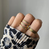 Bague multi-rangs Amandina portée en accumulation (stacking) avec une bague fine tressée sur une main avec pull léopard.