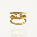 Bague large ouverte effet triple rangs en acier inoxydable doré avec finition texturée et striée sur fond blanc.