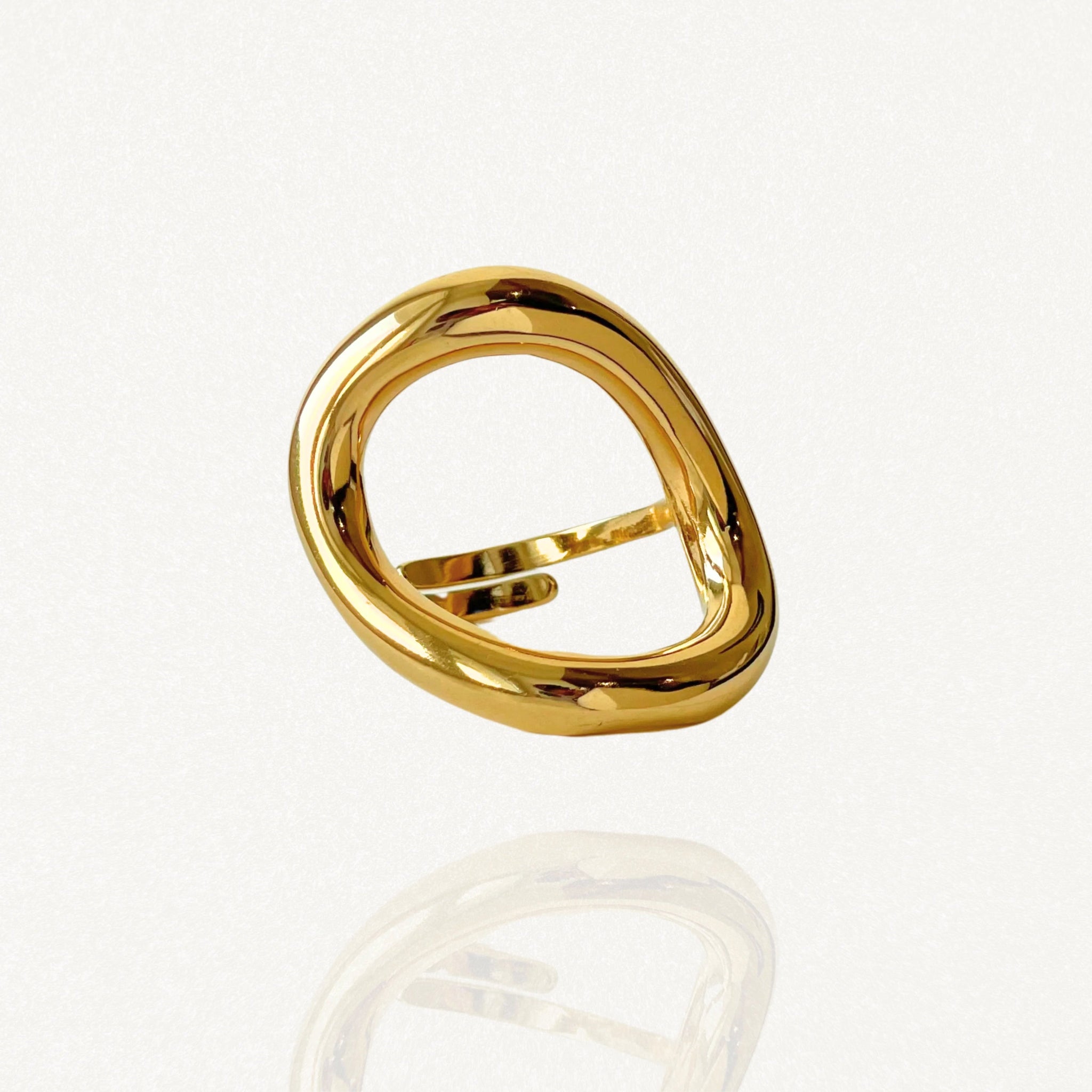Bague large géométrique forme cercle organique et évidé en acier inoxydable doré sur fond blanc.