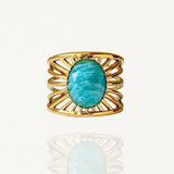Bague large en acier inoxydable doré ornée d'une pierre naturelle Amazonite ovale et motifs rayons de soleil ajourés sur fond blanc.