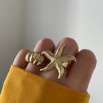 Bague Aurora portée en accumulation (stacking) avec une bague statement étoile de mer dorée.