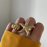 Bague Aurora portée en accumulation (stacking) avec une bague statement étoile de mer dorée.
