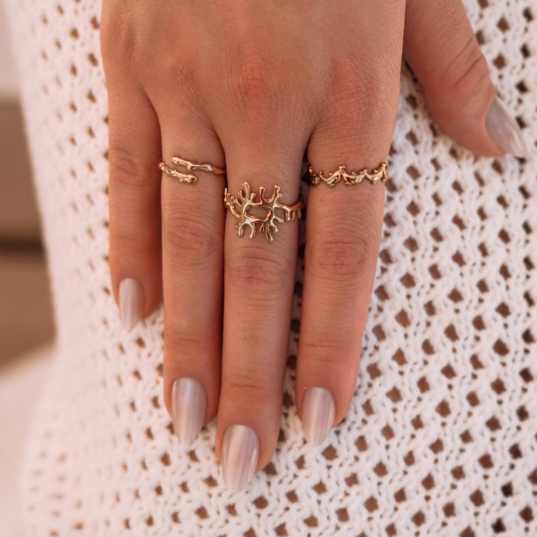 Bagues en acier inoxydable doré: design bague corail central, bague branche et bague vague sur une main.