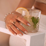 Main de femme portant trois bagues en acier inoxydable doré. Motifs fantaisie avec verre de boisson fraîche.