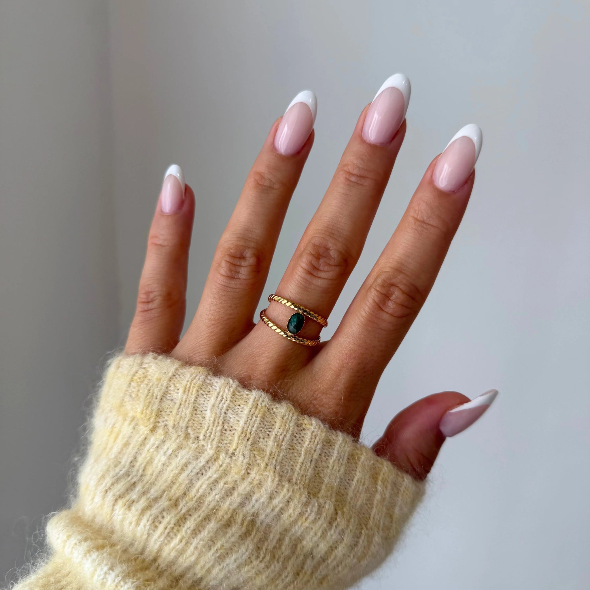 Bague Cataleya dorée avec pierre verte portée au doigt, accessoire élégant avec pull en maille.