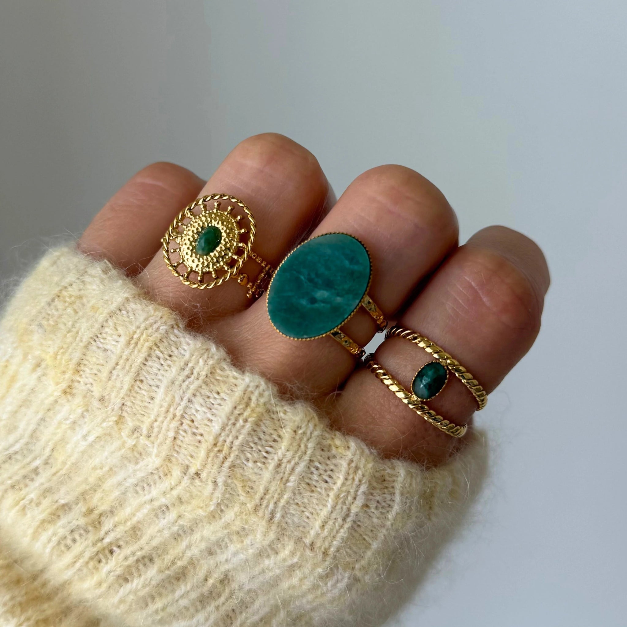 Bague Cataleya portée en accumulation (stacking) avec d'autres bagues dorées et pierres naturelles vertes (style malachite ou aventurine).
