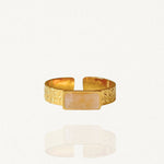 Bague bandeau ajustable en acier inoxydable doré, finition martelée, ornée d'une pierre rectangulaire horizontale beige rosée sur fond blanc.