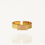 Bague bandeau ajustable en acier inoxydable doré, finition martelée, ornée d'une pierre rectangulaire horizontale beige rosée sur fond blanc.