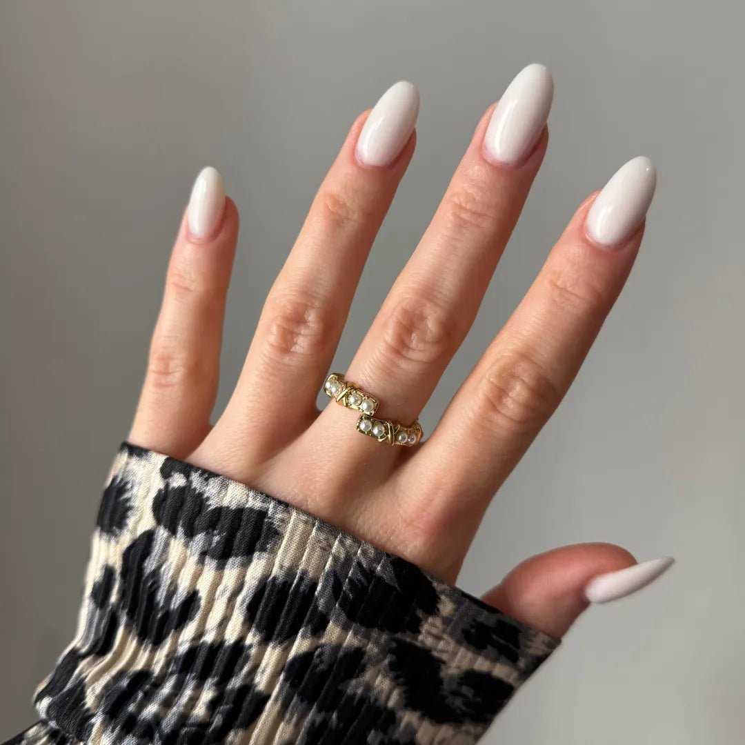 Bague dorée ouverte ornée de petites perles blanches sur annulaire, main aux ongles ovales blancs, manche imprimé léopard.