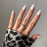 Bague dorée ouverte ornée de petites perles blanches sur annulaire, main aux ongles ovales blancs, manche imprimé léopard.