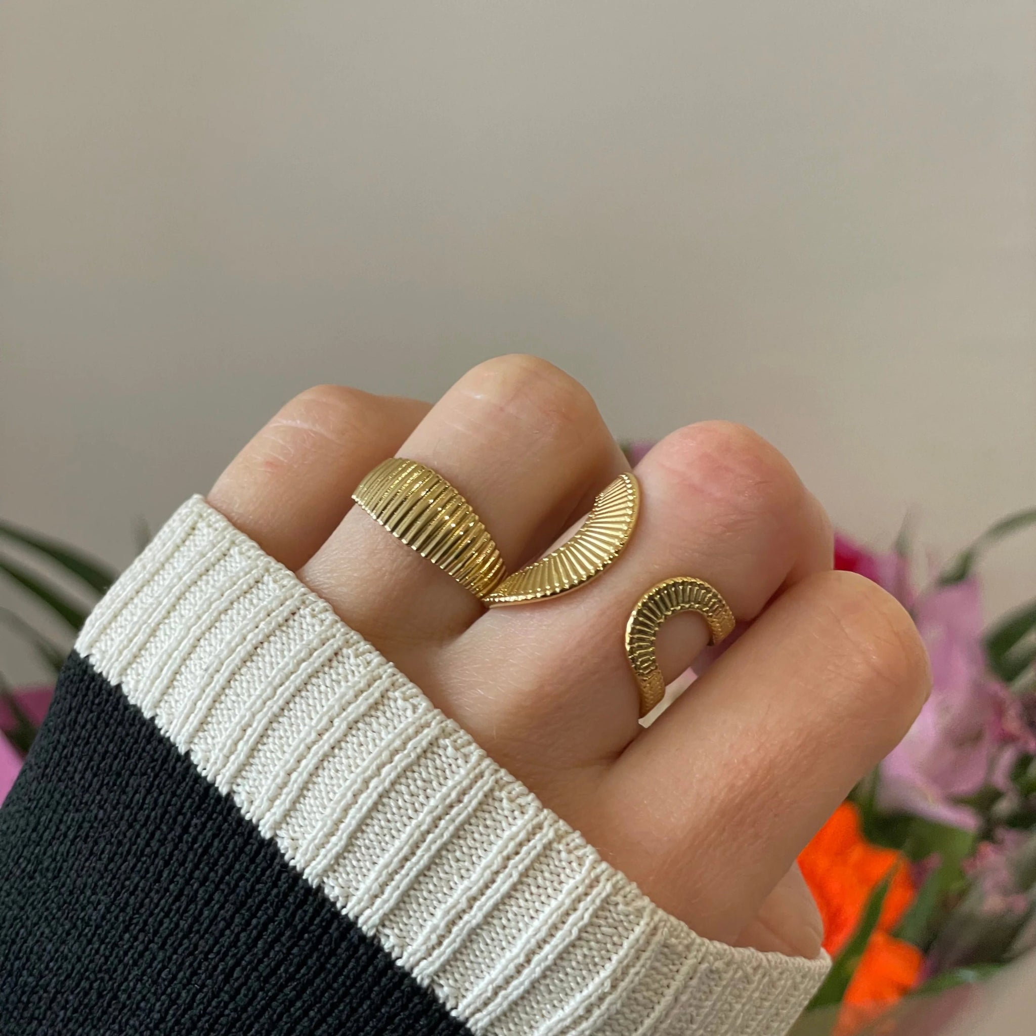 Bague large texturée Claudia portée en accumulation (stacking) avec d'autres bagues dorées.