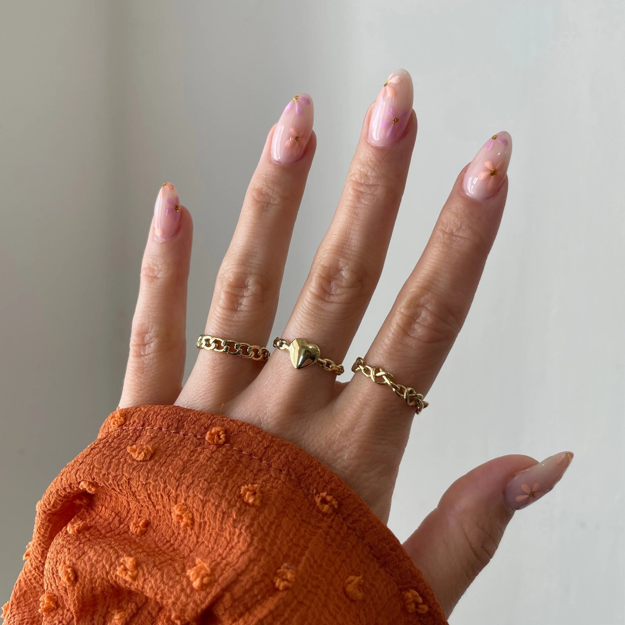 Bague maillons Dakota portée en accumulation (stacking) avec d'autres bagues fines dorées sur une main avec manche rouille.