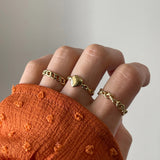 Bague maillons Dakota portée en accumulation (stacking) avec d'autres bagues fines dorées sur une main avec manche rouille.