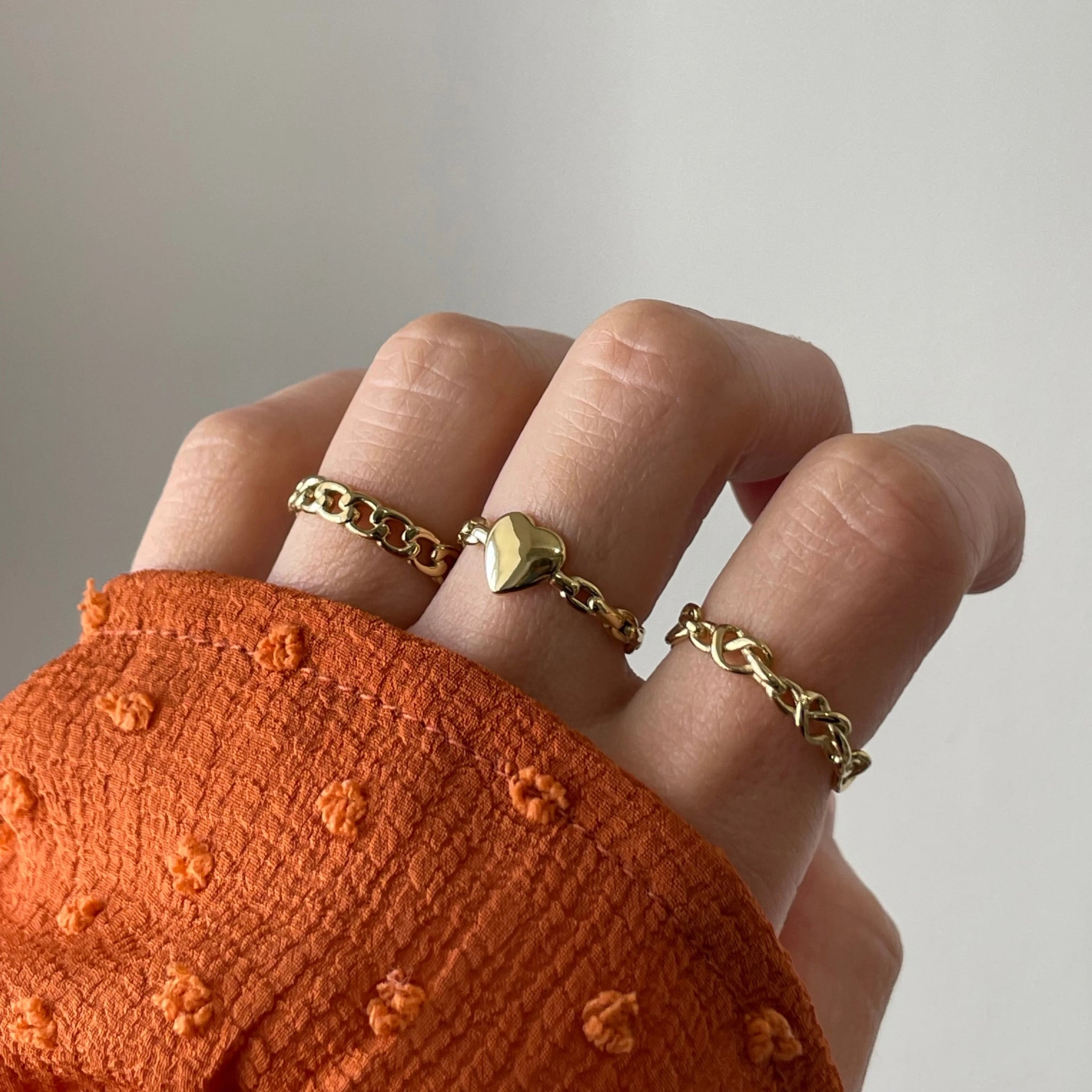 Bague maillons Dakota portée en accumulation (stacking) avec d'autres bagues fines dorées sur une main avec manche rouille.