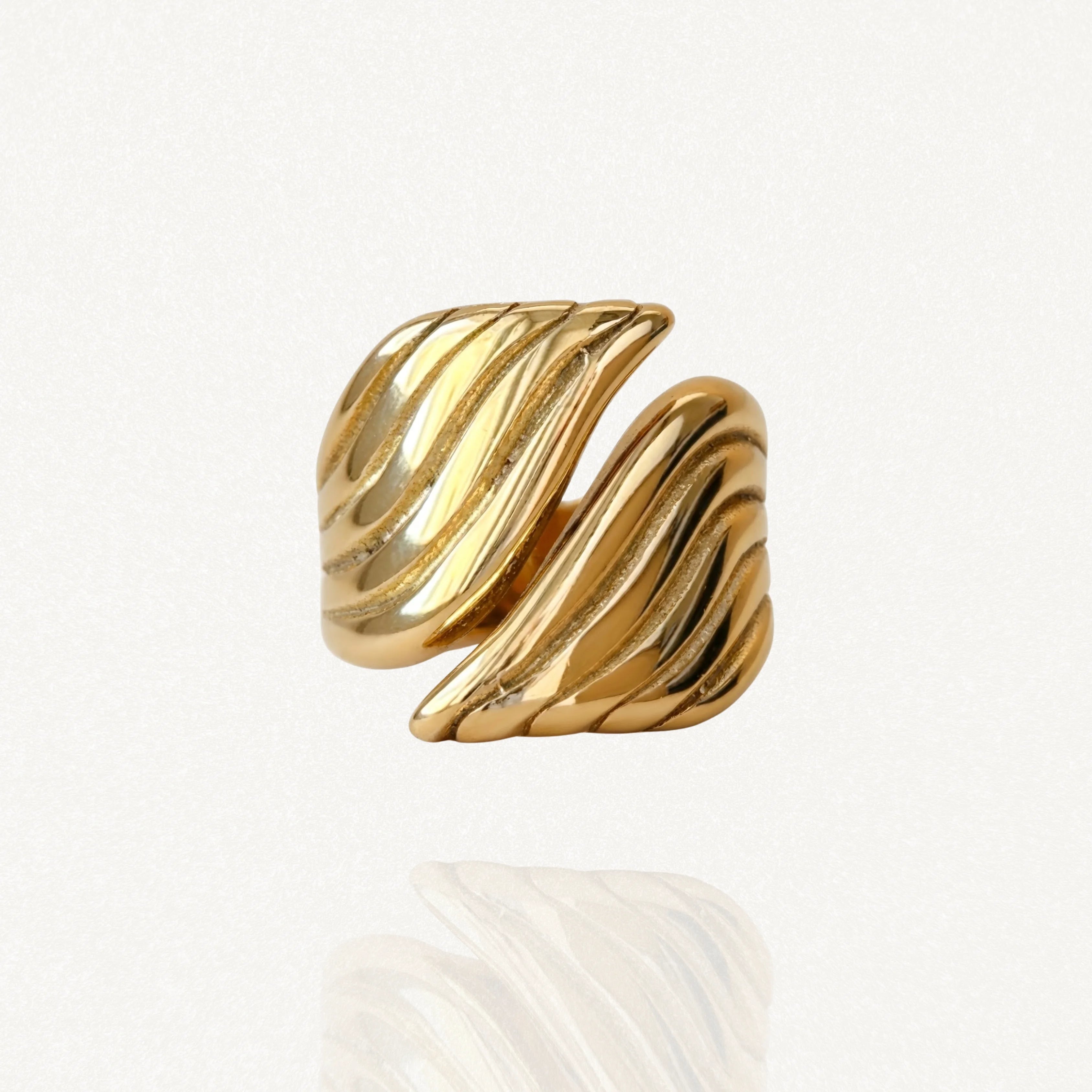 Bague dorée épaisse avec un design sculptural et texturé rappelant une feuille ou une aile, vue de face sur fond blanc.