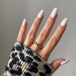 Main féminine avec bague dorée à maillons sur l'annulaire. Ongles longs ovales laiteux. Manchette imprimé léopard.