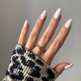 Main féminine avec bague dorée à maillons sur l'annulaire. Ongles longs ovales laiteux. Manchette imprimé léopard.