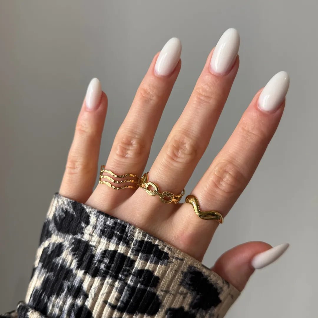 Main femme aux ongles ovales blancs, 3 bagues dorées: triple vague, chaînes entrelacées, ondulée. Manche imprimé animal B&W.