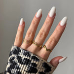 Main femme aux ongles ovales blancs, 3 bagues dorées: triple vague, chaînes entrelacées, ondulée. Manche imprimé animal B&W.