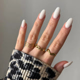 Main femme aux ongles ovales blancs, 3 bagues dorées: triple vague, chaînes entrelacées, ondulée. Manche imprimé animal B&W.