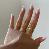 Bague bandeau Enora portée en accumulation (stacking) avec d'autres bagues fines dorées sur une main.
