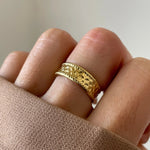 Gros plan bague Enora dorée à relief martelé portée au doigt, style classique et lumineux.