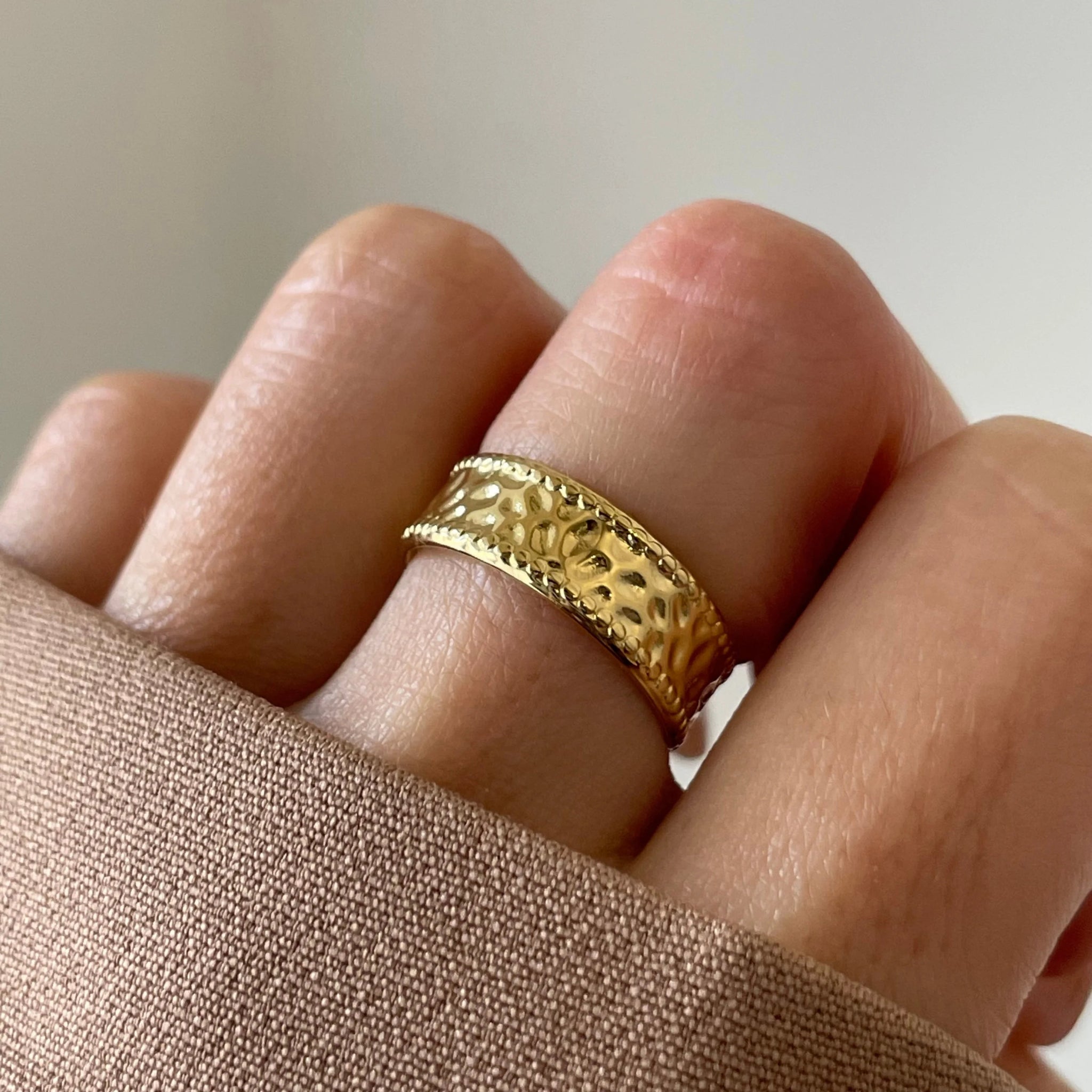 Gros plan bague Enora dorée à relief martelé portée au doigt, style classique et lumineux.
