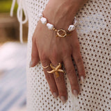 Bague en acier inoxydable doré, motif étoile de mer, portée sur une main féminine.