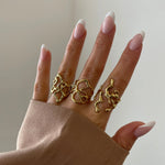 Bague Flora portée en accumulation (stacking) avec d'autres bagues graphiques dorées sur une main manucurée.
