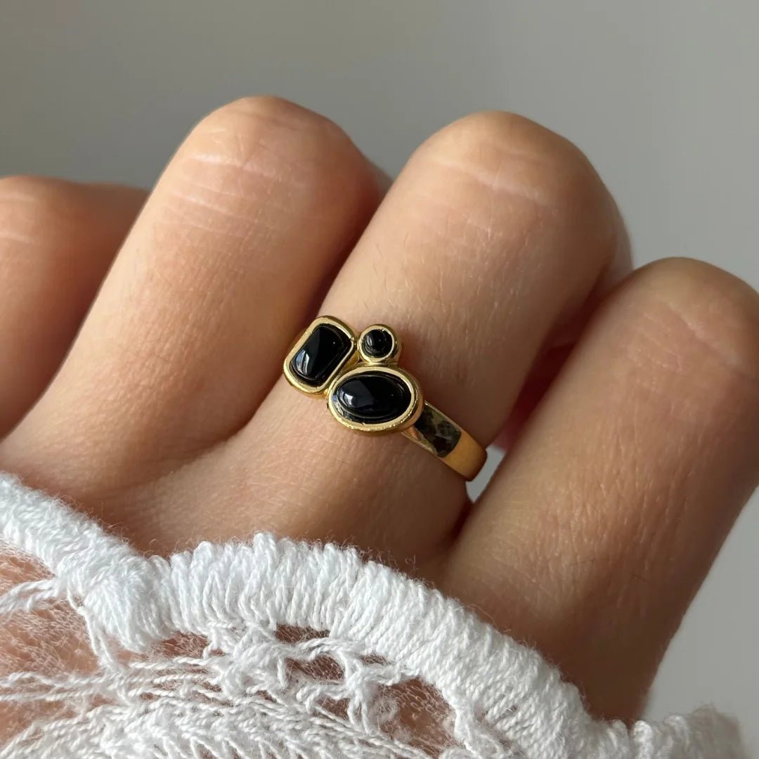 Gros plan bague Inès à pierres noires style onyx portée au doigt, contraste chic avec une manche en dentelle blanche.