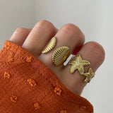 Bague coquillage Jana portée en accumulation (stacking) avec une bague étoile de mer pour un look sirène complet.