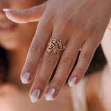 Bague en acier inoxydable doré, motif marin détaillé : hippocampe, corail, étoile de mer, portée sur une main.