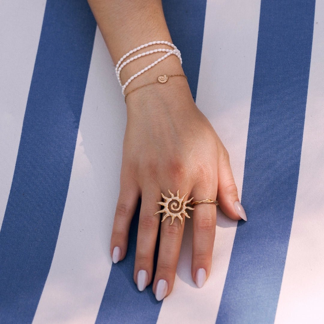 Bague soleil stylisée en acier inoxydable doré avec spirale et rayons, portée sur une main féminine.