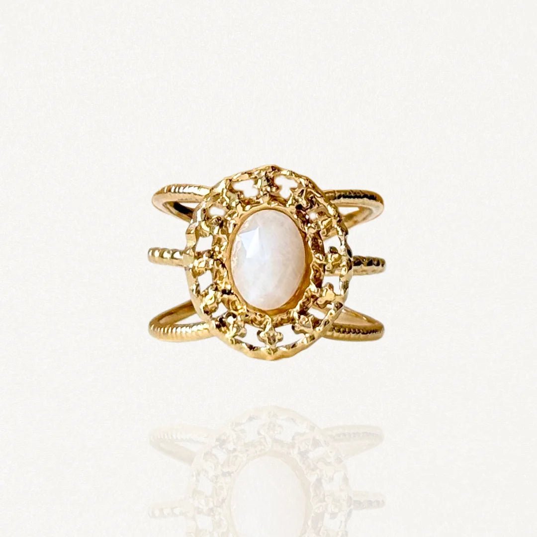 Bague large en acier inoxydable doré avec pierre blanche ovale et contour travaillé façon dentelle ou filigrane.