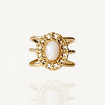 Bague large en acier inoxydable doré avec pierre blanche ovale et contour travaillé façon dentelle ou filigrane.