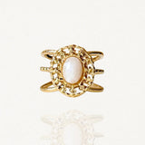 Bague large en acier inoxydable doré avec pierre blanche ovale et contour travaillé façon dentelle ou filigrane.