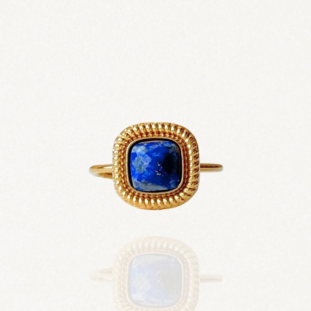 Bague en acier inoxydable doré ornée d'une pierre carrée bleue nuit intense (style Lapis Lazuli) et contour perlé sur fond blanc.