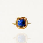 Bague en acier inoxydable doré ornée d'une pierre carrée bleue nuit intense (style Lapis Lazuli) et contour perlé sur fond blanc.