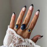 Bague Lucie portée en accumulation (stacking) avec d'autres bagues dorées serties de pierres bleues naturelles.