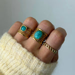 Bague Athena portée en accumulation (stacking) avec d'autres bagues dorées à pierres naturelles turquoises.